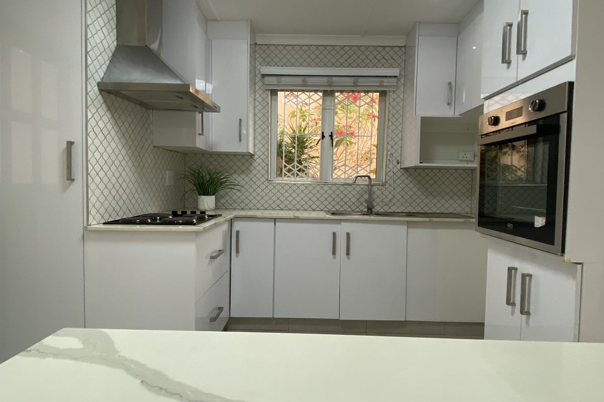 Modern kitchen featuring white cabinetry, stone countertops, stainless steel appliances, and a decorative tiled backsplash with ample storage and task lighting.