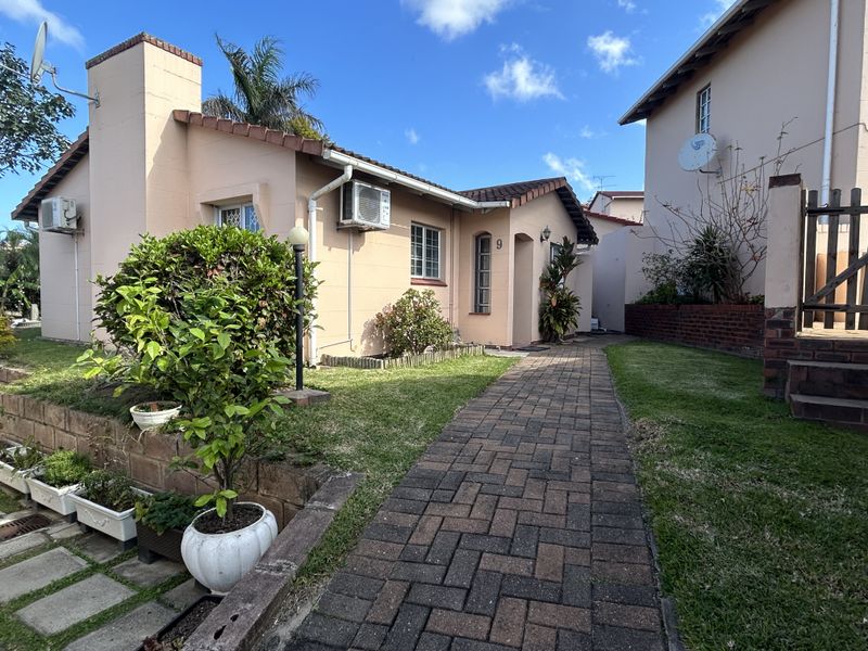 Front view of a townhouse featuring a paved walkway, landscaped garden, and brick retaining wall, showcasing the property's exterior facade and entrance.