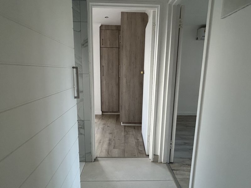 A bright hallway featuring modern wood-look laminate flooring, built-in storage cupboards, and clean white finishes connecting multiple rooms.