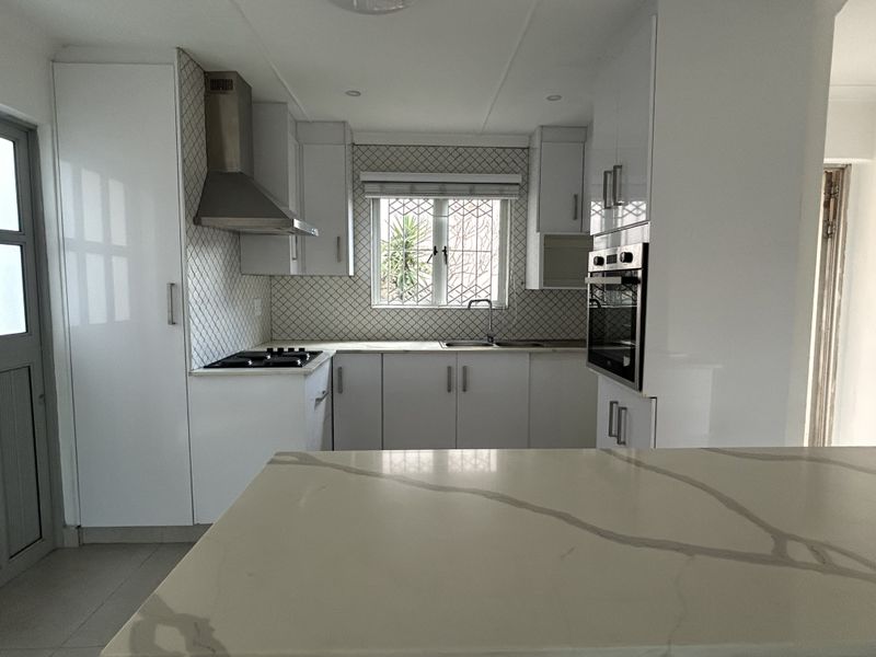 Modern kitchen featuring white cabinetry, stone countertops, built-in oven, gas hob, and a stylish tiled backsplash with ample natural light.
