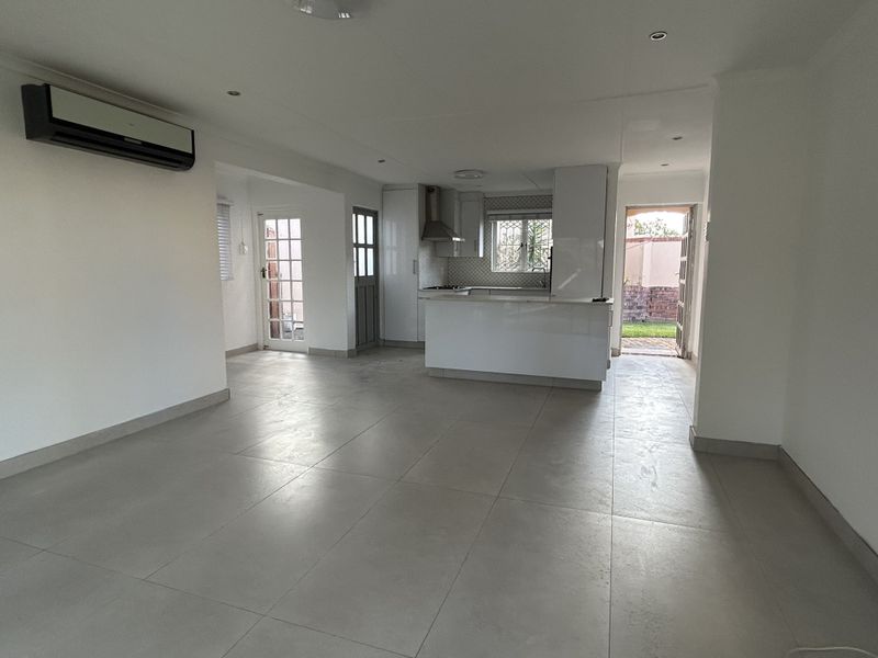Spacious open-plan living and kitchen area featuring modern tiled flooring, built-in cabinetry, and direct access to the exterior through french doors.