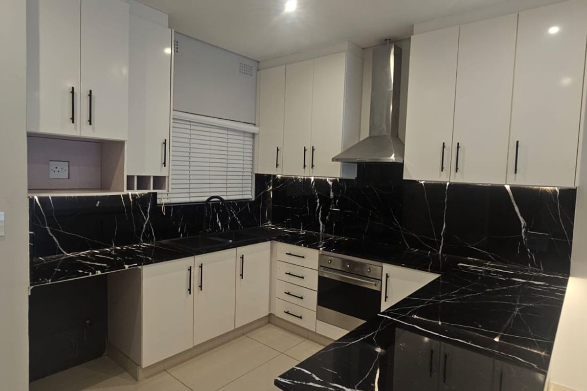 Modern kitchen featuring sleek white cabinetry, striking black marble-look countertops, integrated stainless steel appliances, and contemporary under-cabinet lighting.