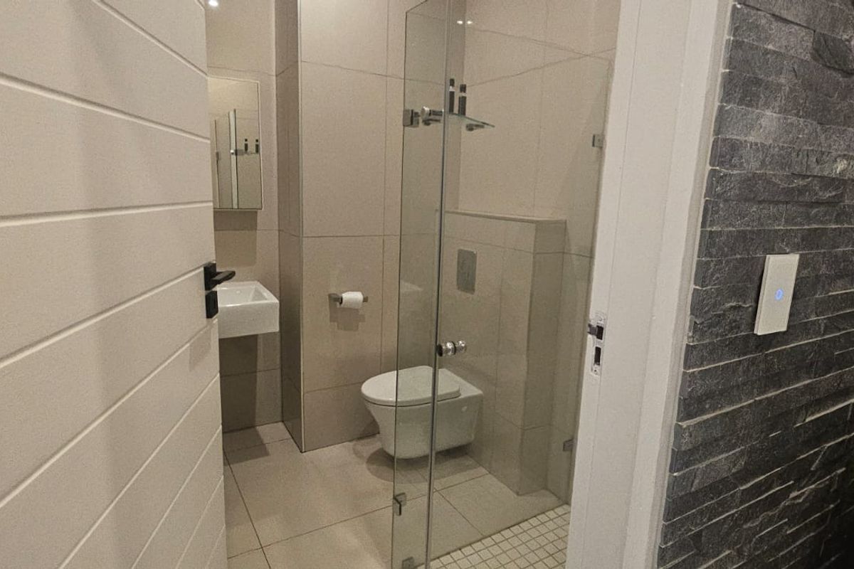 Modern bathroom featuring a wall-hung toilet, glass shower enclosure, wall-mounted basin, and a striking stone feature wall.