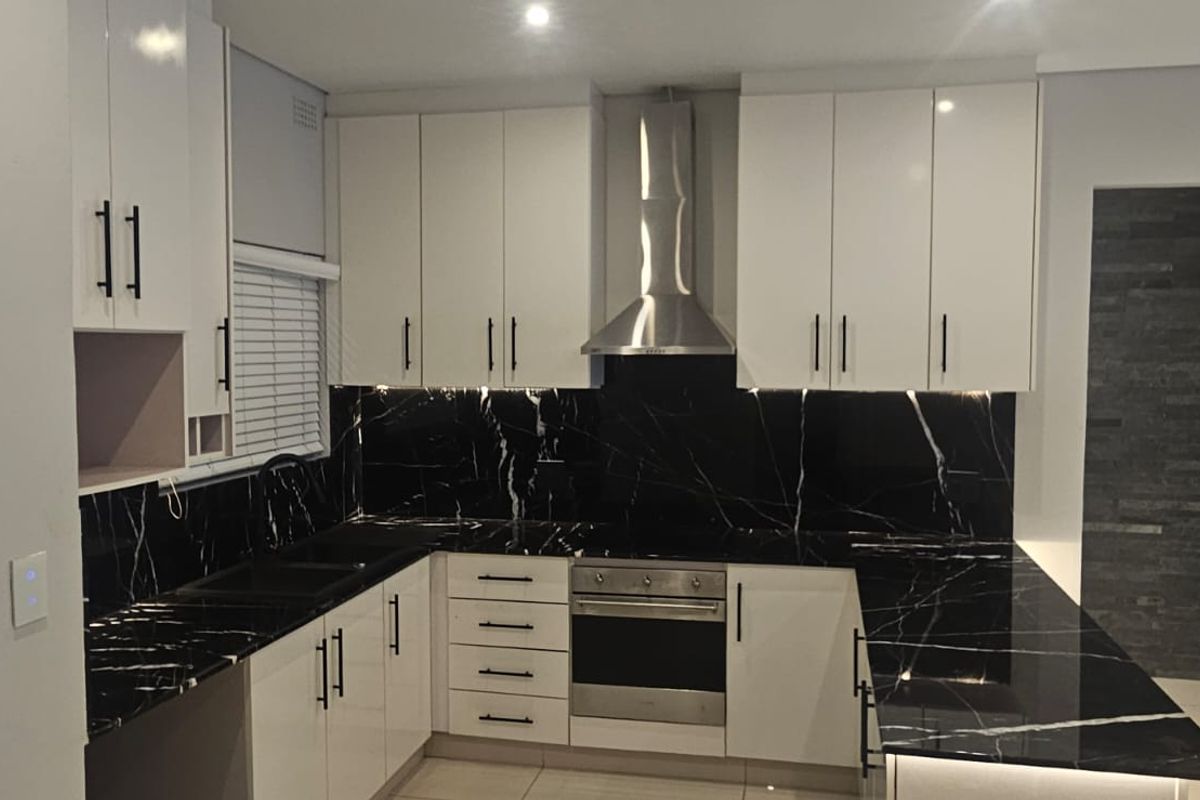 Modern kitchen featuring high-gloss white cabinetry, striking black marble-look countertops, integrated stainless steel appliances, and sleek under-cabinet lighting.