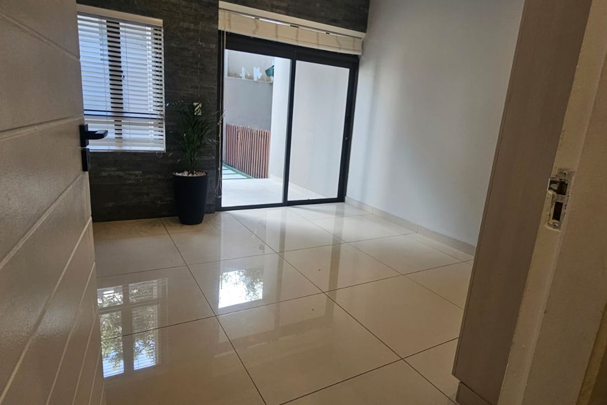 A bright, empty living area featuring polished porcelain floor tiles, a modern stone feature wall, and sliding glass doors leading to an outdoor space.