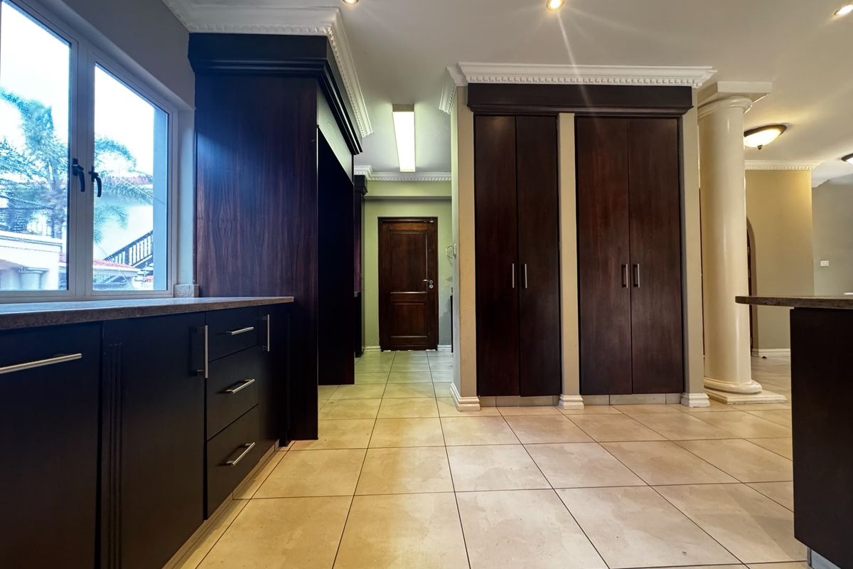 Spacious kitchen area featuring dark wood cabinetry, tiled flooring, and decorative crown molding, offering a clean and functional layout with ample storage space.