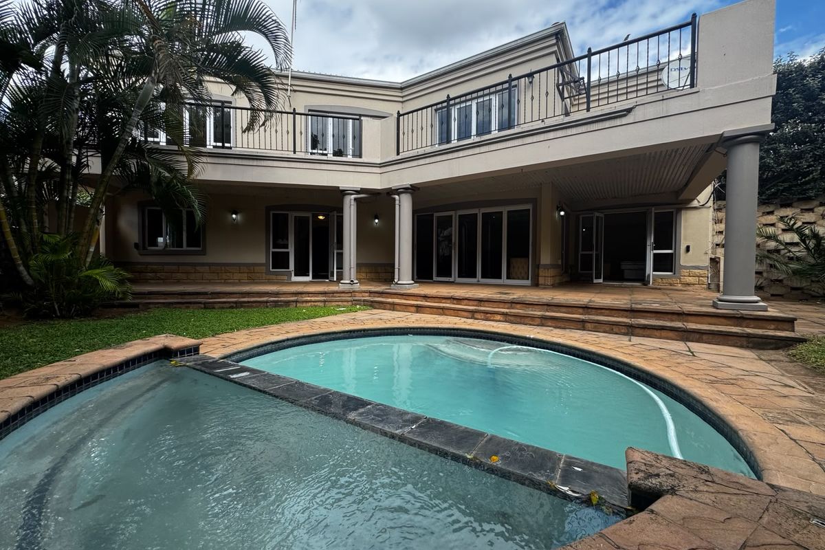 Rear view of a two-story house featuring a swimming pool, covered patio area, and an upper-level balcony with wrought iron railings.