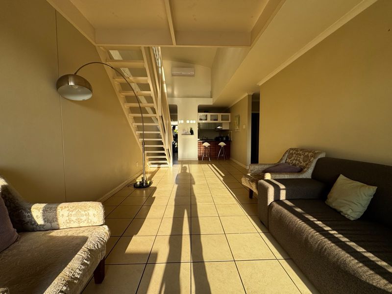 Open-plan living area featuring tiled flooring, a staircase leading to an upper level, and a functional kitchen space with a breakfast bar.