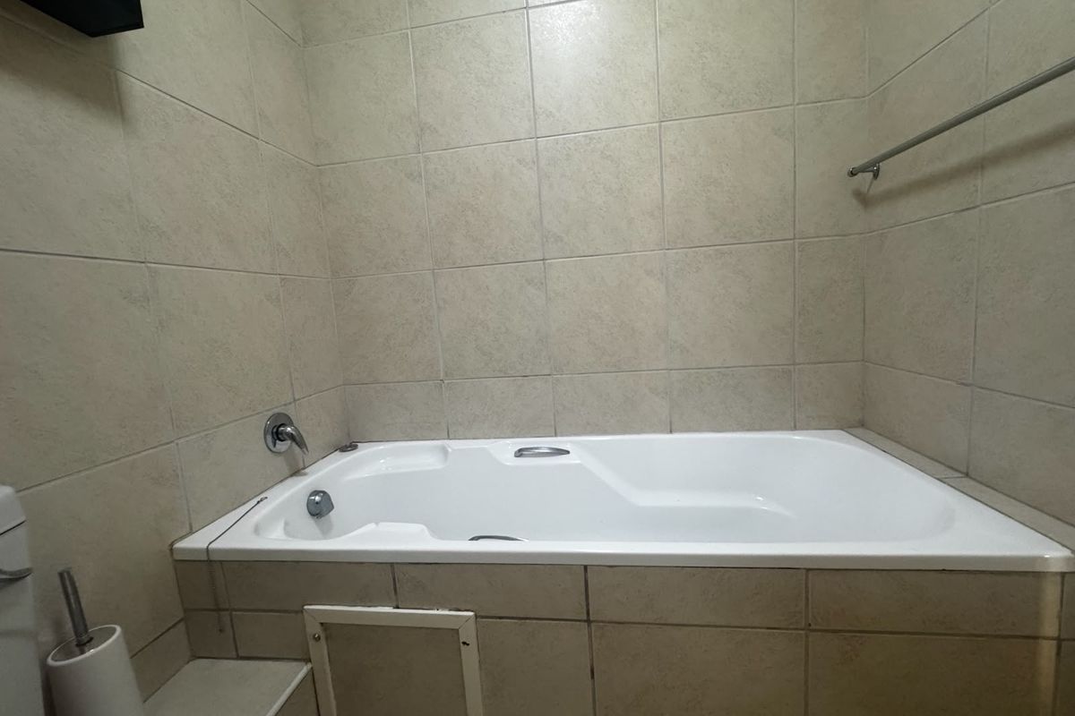 A functional bathroom featuring a built-in bathtub with neutral wall tiling and chrome fixtures, offering a clean and practical space.