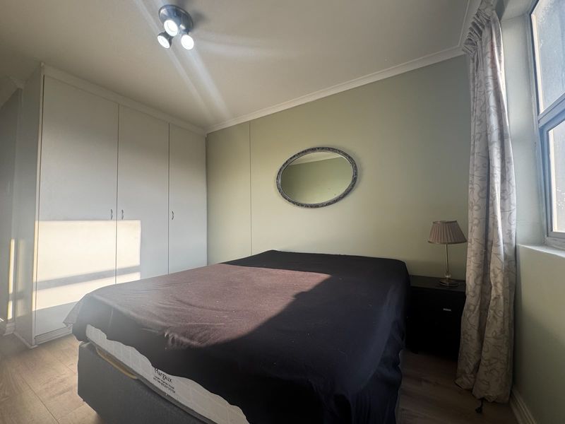 A bedroom featuring built-in cupboards, laminate flooring, and a neutral wall finish, providing a functional and well-lit sleeping space.