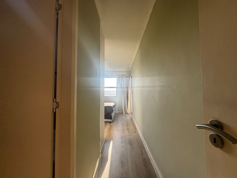 A narrow hallway with light-toned laminate flooring leading towards a bedroom area with natural light.