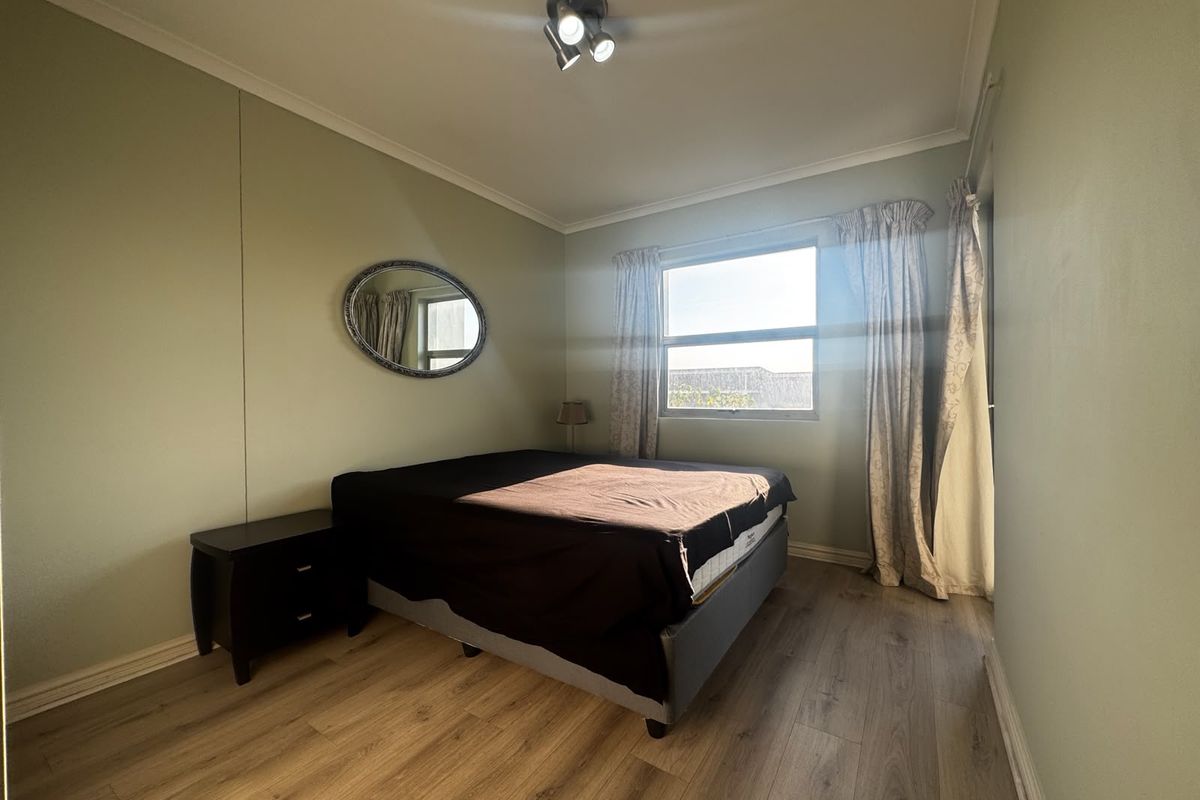 A bedroom featuring light green walls, laminate flooring, and a ceiling-mounted light fixture, providing a functional and neutral living space.