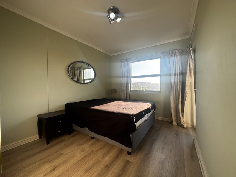 A bedroom featuring light green walls, laminate flooring, and a ceiling-mounted light fixture, providing a functional and neutral living space.