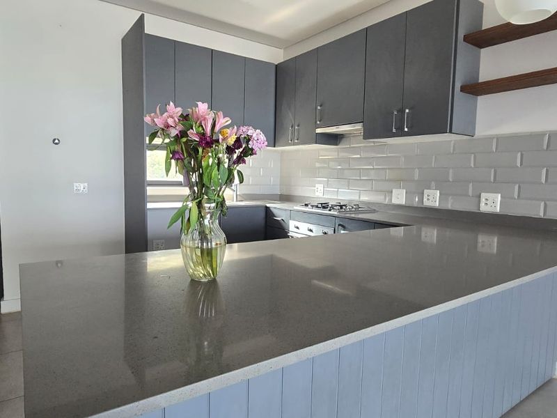 Modern kitchen featuring grey cabinetry, quartz countertops, subway tile backsplash, built-in gas hob, oven, and floating timber shelving.