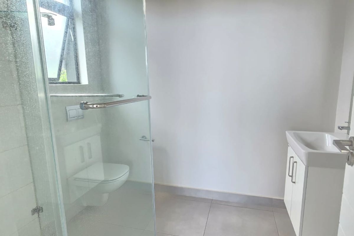A clean, modern bathroom featuring a glass-enclosed shower, wall-mounted toilet, and a compact vanity with basin.