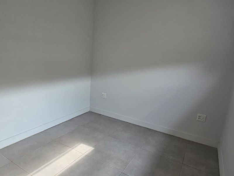 A clean, empty bedroom featuring neutral tiled flooring, white walls, and a modern roller blind, providing a versatile space ready for customization.