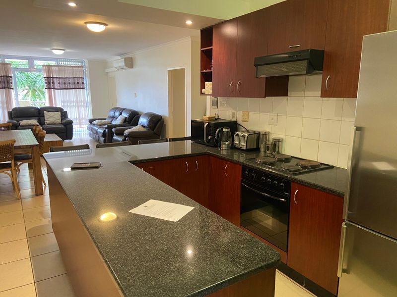 Open-plan kitchen and living area featuring dark wood cabinetry, granite countertops, built-in appliances, and tiled flooring leading to a balcony.