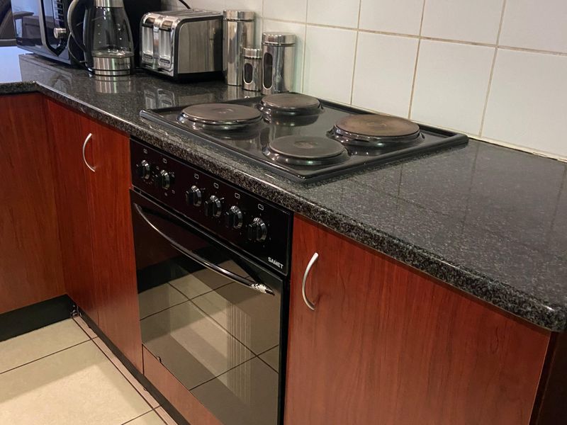 A functional kitchen featuring dark wood-look cabinetry, granite countertops, a built-in oven with an electric hob, and neutral ceramic wall and floor tiling.