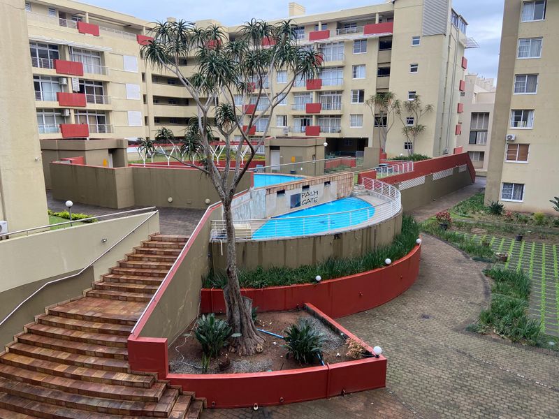 Elevated view of the apartment complex communal pool area featuring paved walkways, landscaped retaining walls, and a central swimming pool.