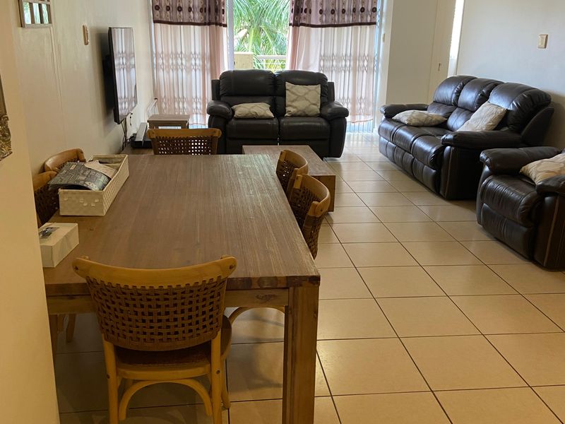 An open-plan living and dining area featuring tiled flooring, a wall-mounted air conditioner, and direct access to a balcony through sliding glass doors.