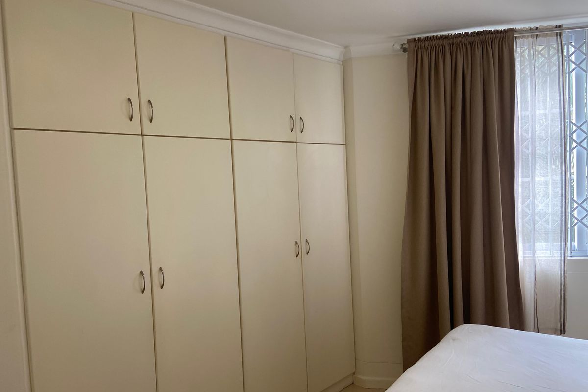 A bedroom featuring floor-to-ceiling built-in cupboards and a window fitted with a security gate.