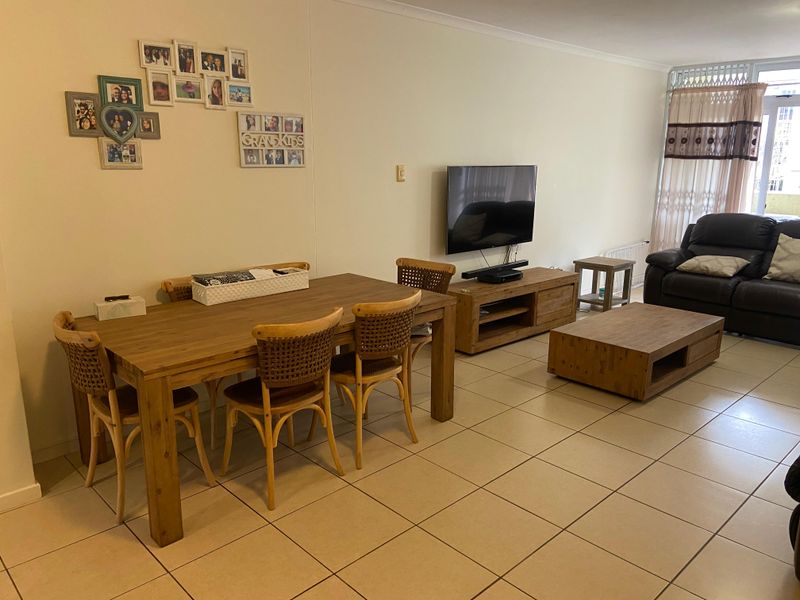 Open-plan living and dining area featuring neutral tiled flooring and access to a balcony through a sliding door with security gate.