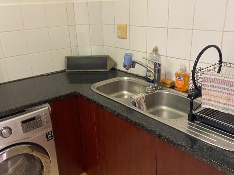 A functional laundry area featuring a stainless steel double sink, granite countertops, tiled splashback, and built-in cabinetry with space for a washing machine.