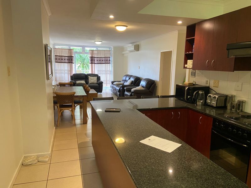 Open-plan living area featuring a kitchen with granite countertops, built-in cabinetry, and integrated appliances, flowing into a dining and lounge space with balcony access.