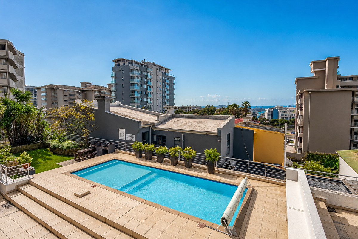 Elevated outdoor pool area featuring a tiled deck, built-in barbecue, and metal safety railings, set against an urban apartment complex backdrop.