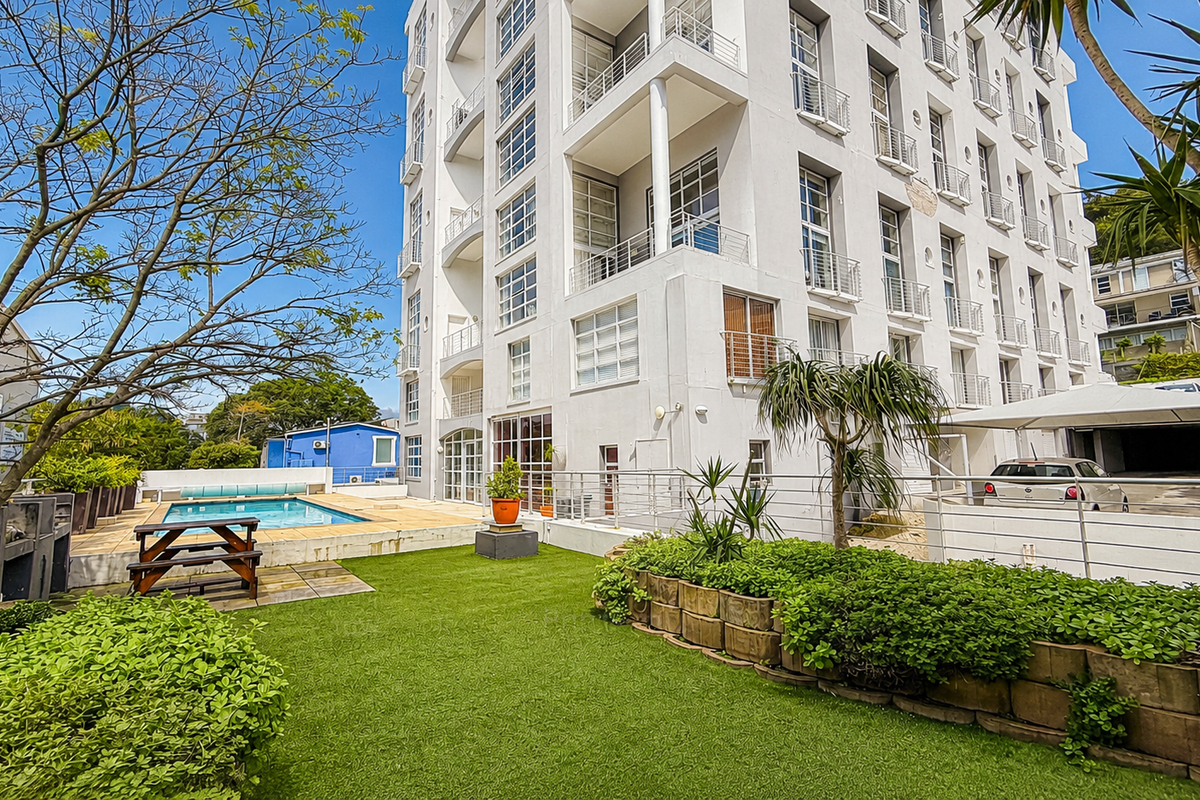 Exterior view of the apartment building featuring a communal swimming pool, landscaped garden area, and covered parking facilities.