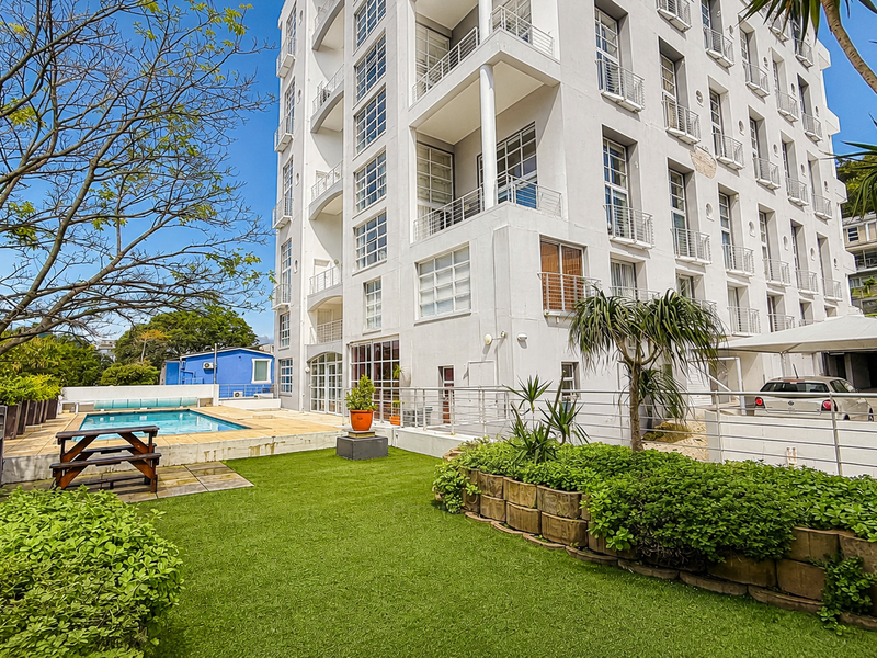 Exterior view of the apartment building featuring a communal swimming pool, landscaped garden area, and covered parking facilities.