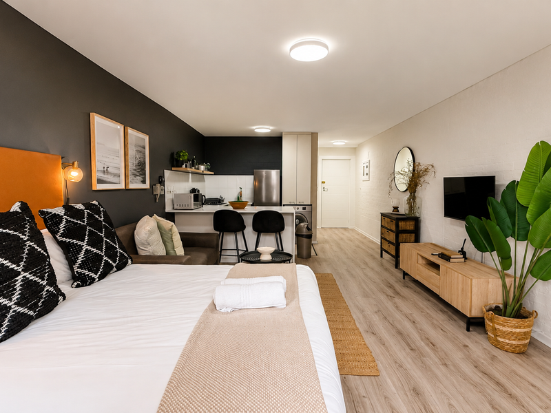 A modern open-plan studio apartment featuring a combined bedroom and kitchen area with laminate flooring and contemporary finishes.