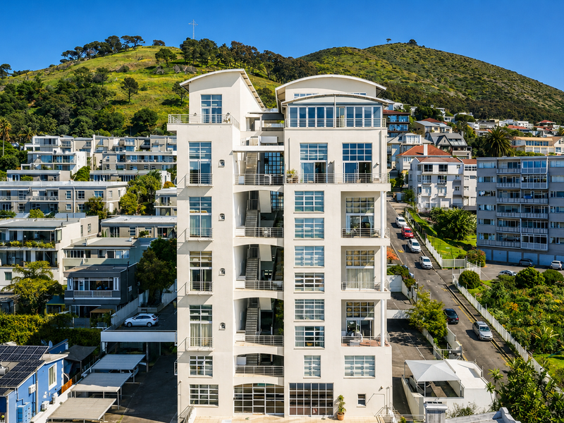 Aerial view of a modern multi-story apartment building featuring a prominent facade with balconies and large windows, set against a scenic hillside backdrop.