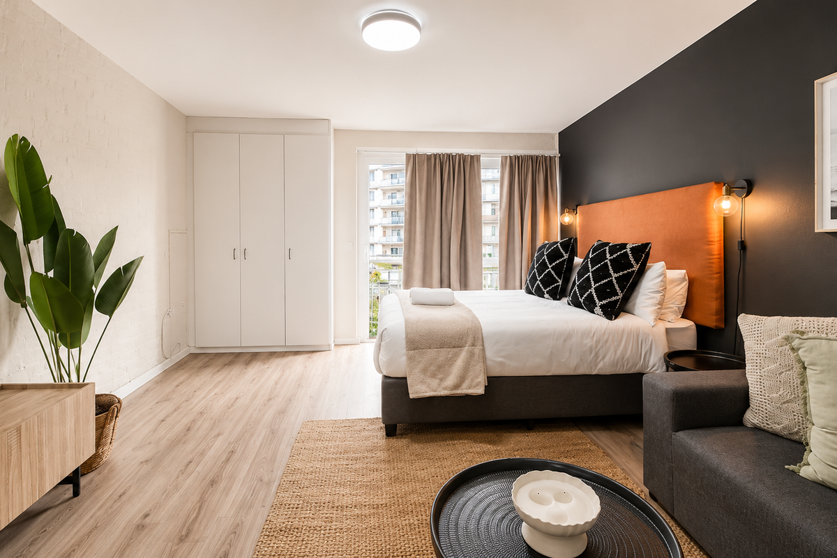A well-maintained bedroom featuring laminate flooring, a built-in wardrobe, an exposed brick feature wall, and direct access to a balcony through sliding glass doors.