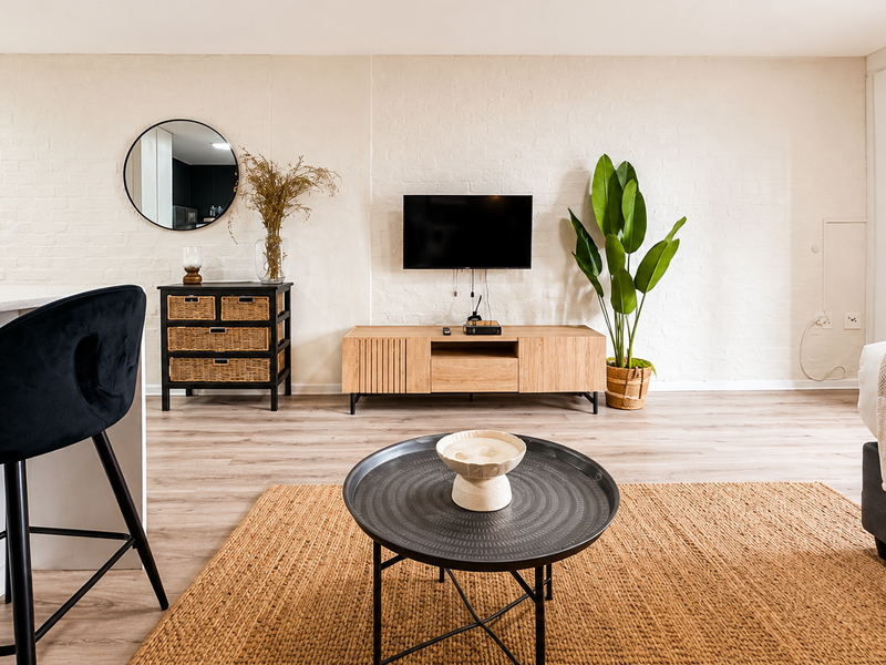 A bright open-plan living area featuring light laminate flooring, a textured painted brick wall, and integrated storage cabinetry.