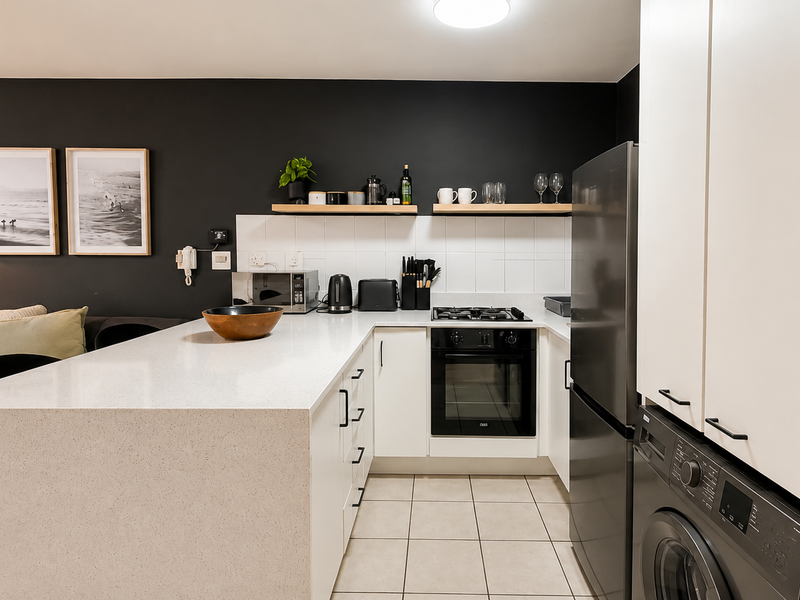 Modern open-plan kitchen featuring quartz countertops, built-in oven, gas hob, and sleek white cabinetry, seamlessly integrated with the living area.