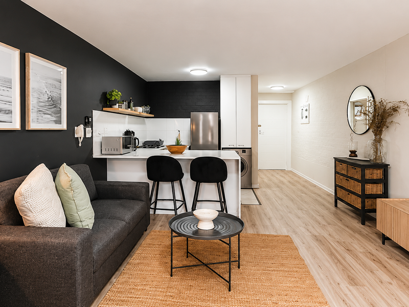 Modern open-plan living area featuring a sleek kitchen with stone countertops, integrated laundry, and a stylish dark feature wall, creating a cohesive living space.