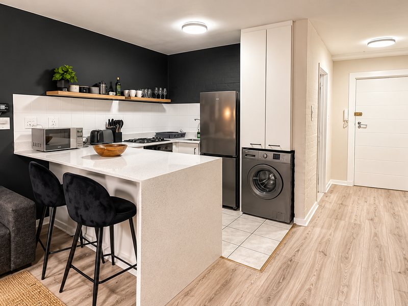 Modern open-plan kitchen featuring quartz countertops, gas hob, and integrated laundry space, seamlessly flowing into the living area with stylish brick wall accents.