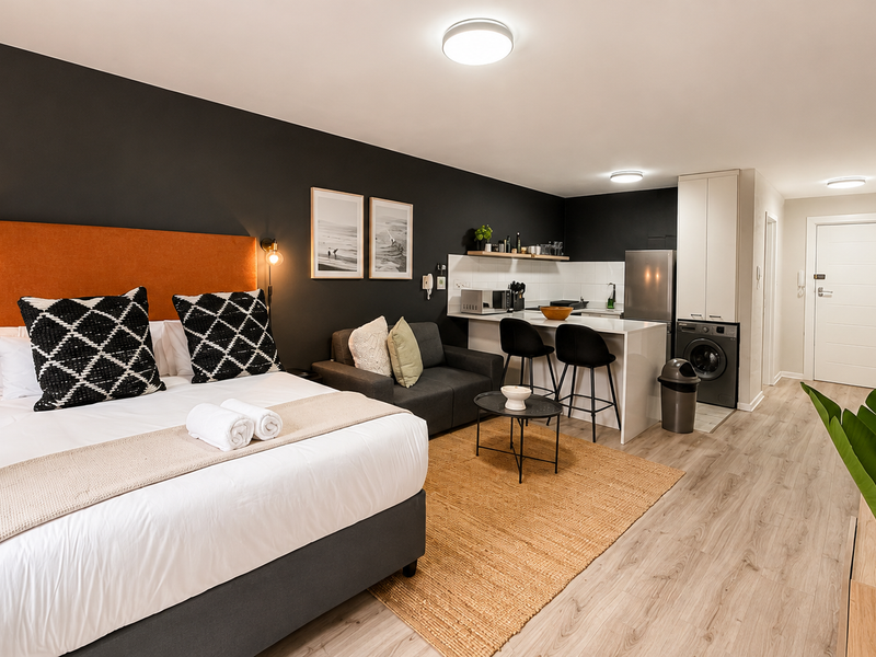 A modern open-plan studio apartment featuring a combined bedroom and kitchen area with a breakfast bar, integrated laundry, and contemporary finishes.