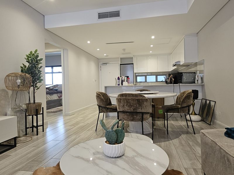 Modern open-plan living and kitchen area featuring sleek cabinetry, stone benchtops, ducted air conditioning, and contemporary tiled flooring throughout.