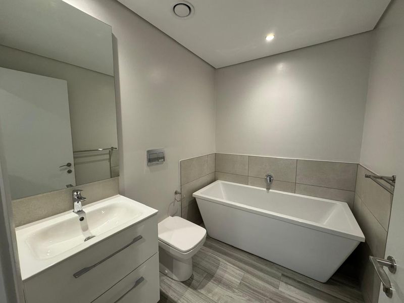 Modern bathroom featuring a sleek freestanding bathtub, wall-hung toilet, vanity with basin, and neutral tile finishes.