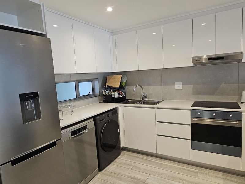 Modern kitchen featuring white gloss cabinetry, stone countertops, integrated appliances, and a sleek tiled backsplash in a clean, contemporary design.