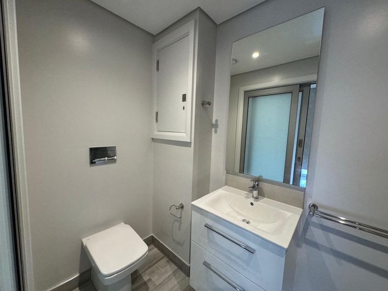 A modern, clean bathroom featuring a wall-mounted toilet, a sleek vanity cabinet with an integrated sink, and a large wall mirror.
