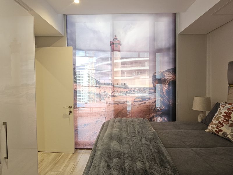 Modern bedroom featuring sleek built-in wardrobes, recessed ceiling lighting, and wood-look laminate flooring, complemented by a large window with a decorative lighthouse blind.