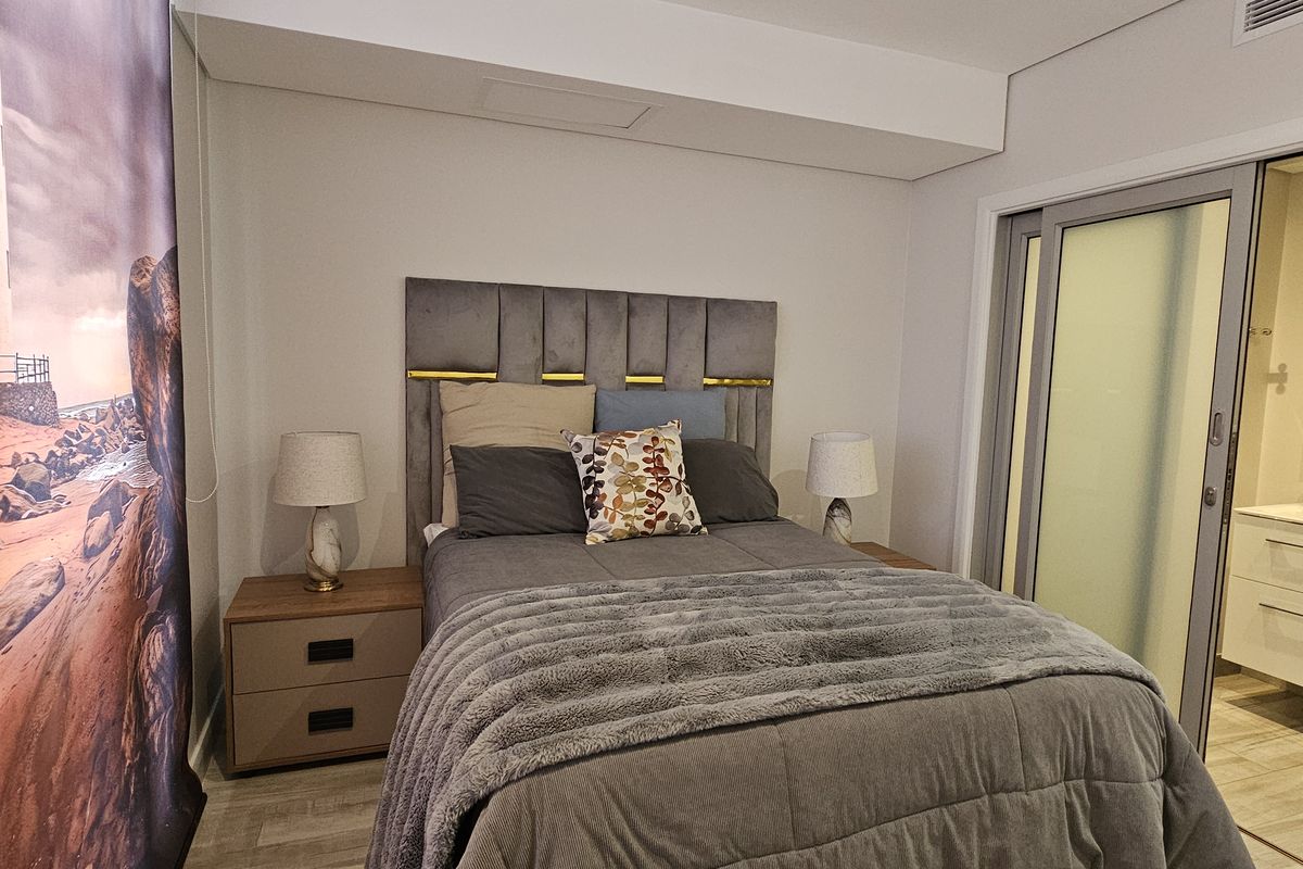 A modern bedroom featuring a neutral color palette, integrated en-suite bathroom access via sliding glass doors, and contemporary finishes.
