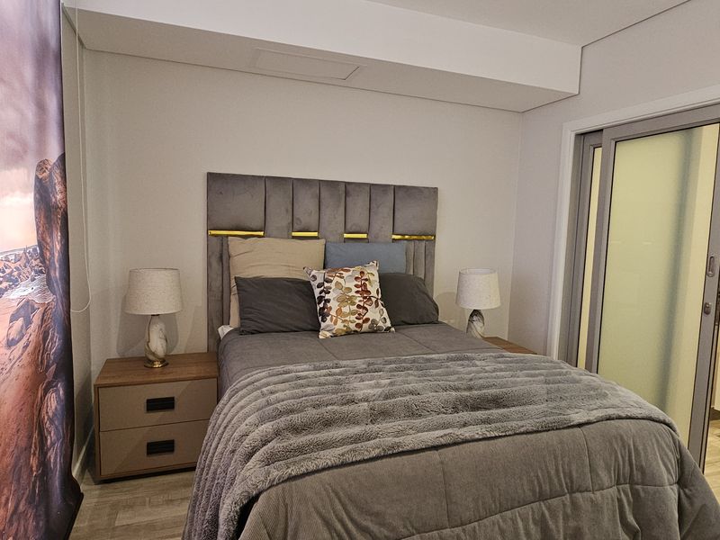 A modern bedroom featuring a neutral color palette, integrated en-suite bathroom access via sliding glass doors, and contemporary finishes.