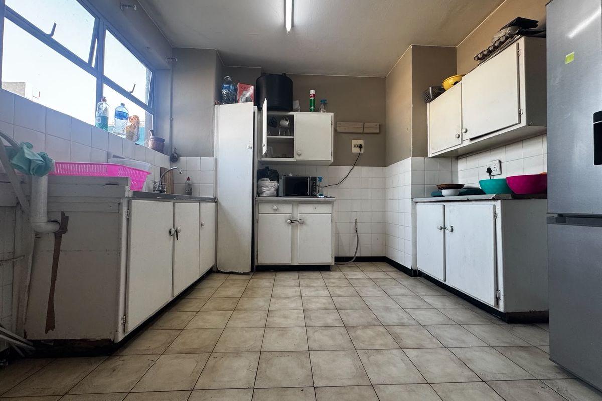 A dated kitchen featuring tiled flooring, white built-in cabinetry, and tiled splashbacks, offering significant potential for a modern renovation.
