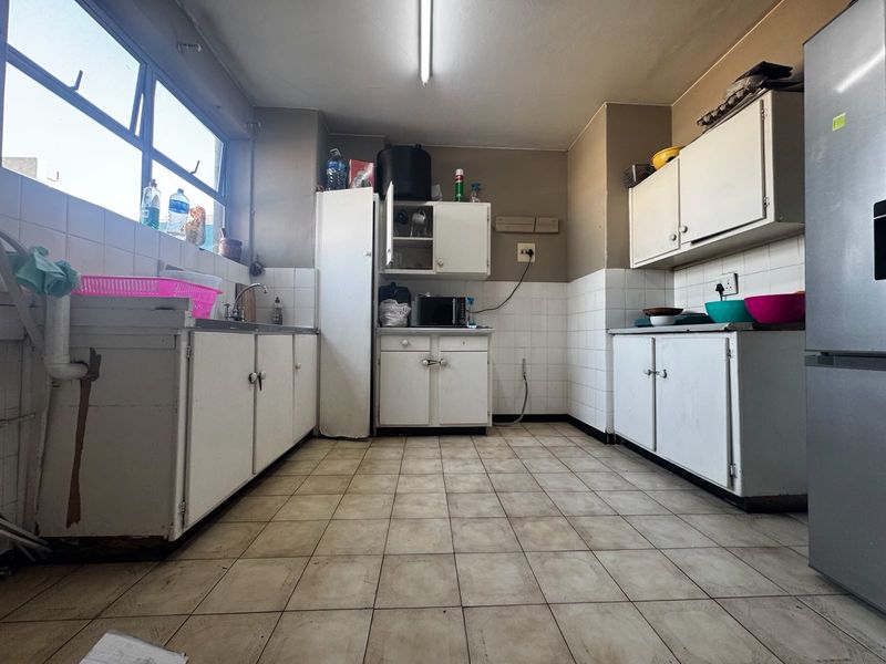 A dated kitchen featuring tiled flooring, white built-in cabinetry, and tiled splashbacks, offering significant potential for a modern renovation.
