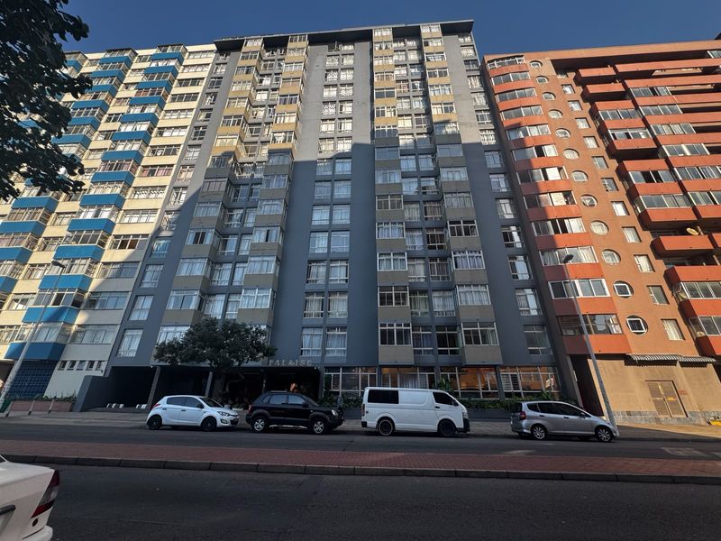 Street-level view of a multi-story apartment building facade featuring numerous enclosed balconies and a central entrance.