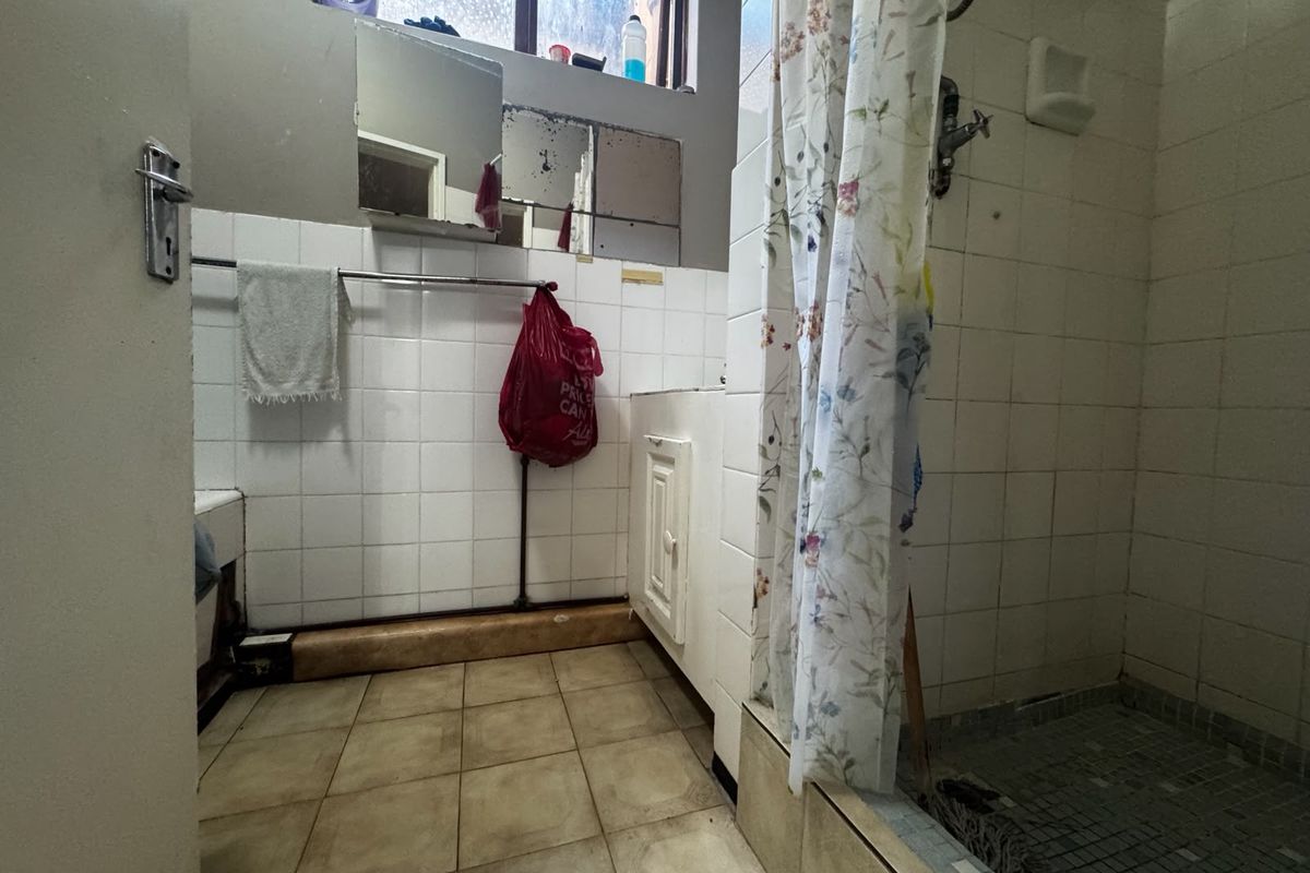 A dated bathroom featuring a shower, vanity unit, and tiled finishes, currently requiring maintenance and cosmetic updates to improve its overall condition.